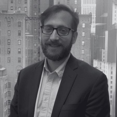A man with glasses and a beard wearing a suit.