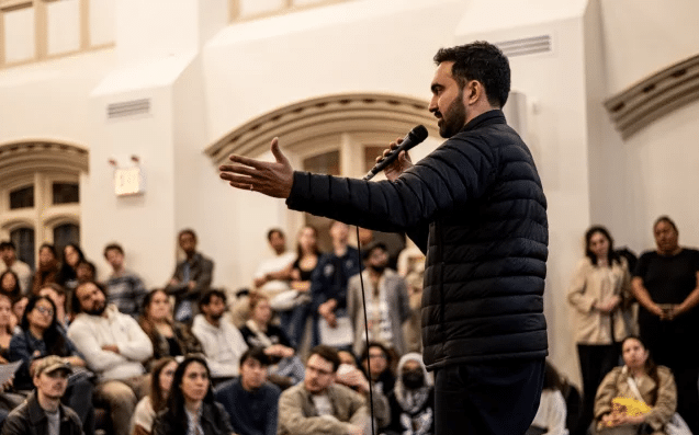 A man speaking into a microphone in front of a crowd.