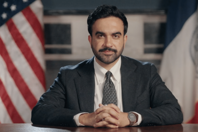 A man sitting at a desk with American and French flags behind him.